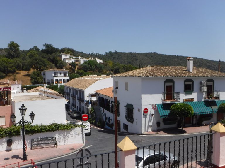 'White houses and tiled roofs in the village of Benahavís with wooded hills behind'