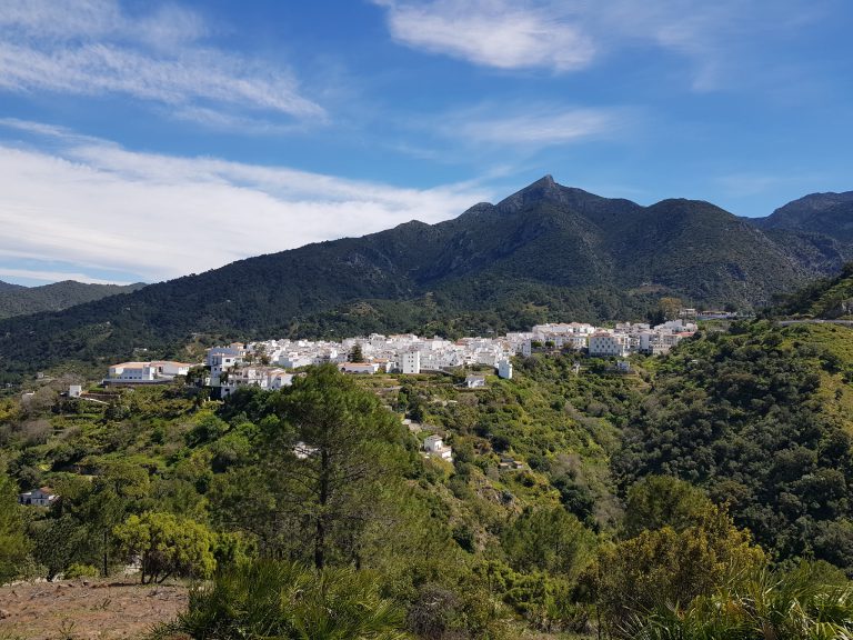 'The white village of Istán on a green hillside below the peaks of the Sierra de las Nieves'