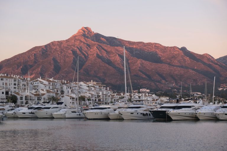 'Yachts moored in the Puerto Banús marina, with La Concha lit by the evening sun behind'