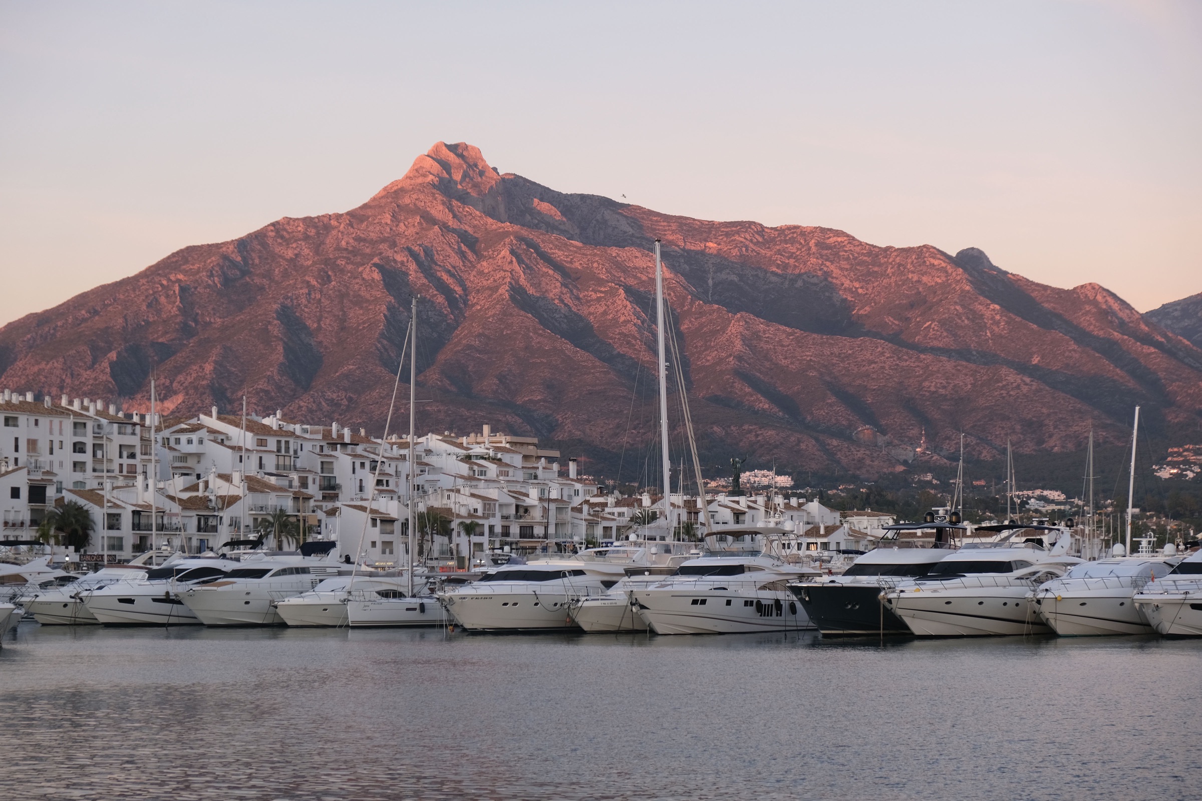 Yates amarrados en el puerto deportivo de Puerto Banús, con La Concha iluminada por el sol del atardecer al fondo