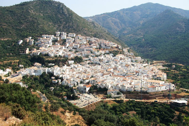 'The white village of Ojén spread across a green hillside below wooded mountains'